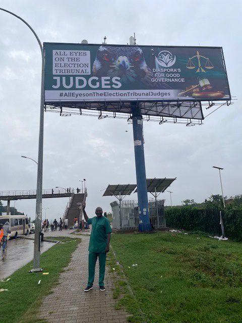 All Eyes on the Judiciary billboard. Attorney Emmanuel Ogebe, TruthNigeria contributor, standing underneath in Abuja. Courtesy, Emmanuel Ogebe.