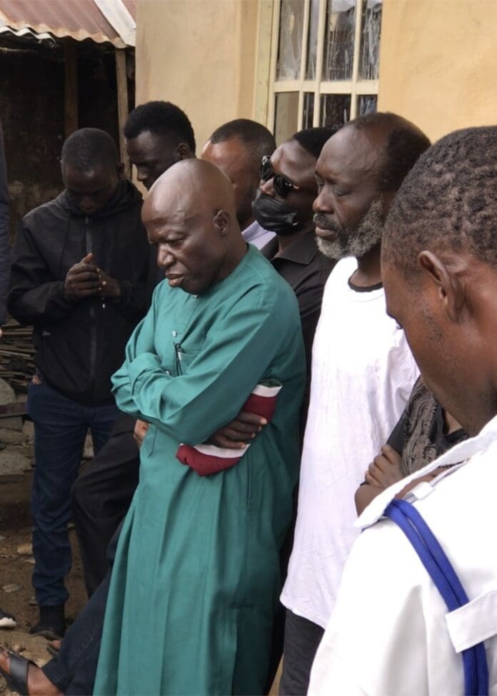 A Father’s Grief: Mr. Joseph Danbako (in green, second from left in front) hugs himself as he watches his son’s body being lowered into the grave on July 15. All photos by Masara Kim.