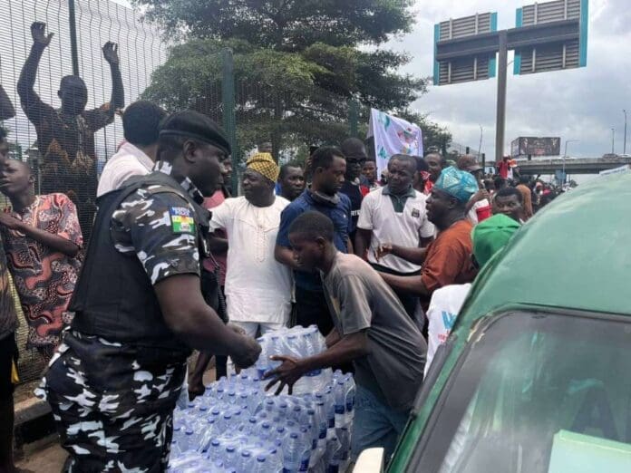 A Nigeria Police Officer, in a rare show of friendship, giving out bags of bottle water to #EndBadGovernance Protesters in Ojota, Lagos, South West Nigeria, Sunday. (Credit: Olatunde Marolan)