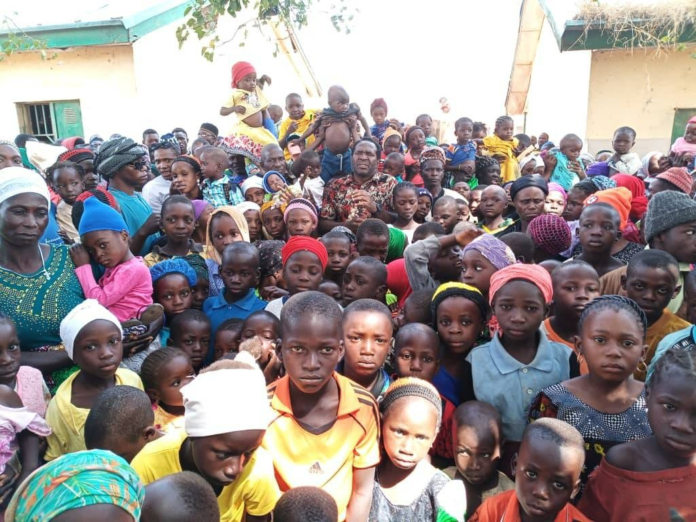 Women and children displaced from their villages in Kajuru County gather around reporter Mike Odeh James (top center) on Jan. 6, 2025. The children are among 7,000 displaced people who have sought shelter with friendly communities within their tribal circle. Most are reportedly without food. Credit: Mike Odeh James.