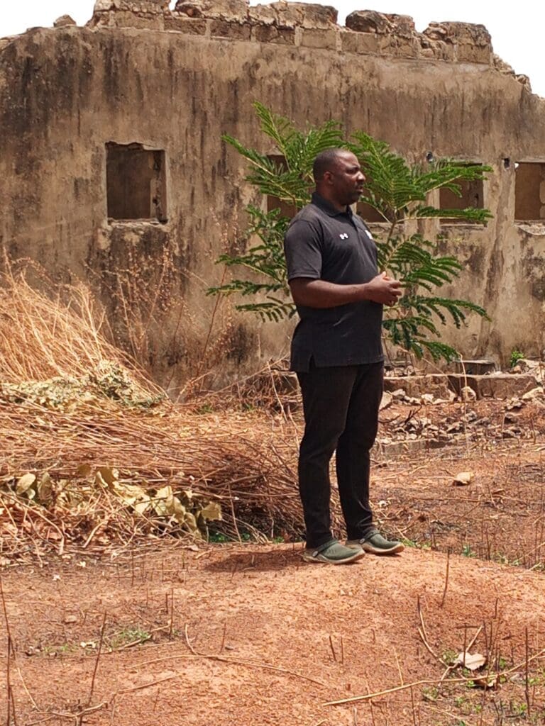David Madami, a lecturer with Kaduna state College of Education stands by his former primary school in Rumana, Monday (Credit: Luka Binniyat).